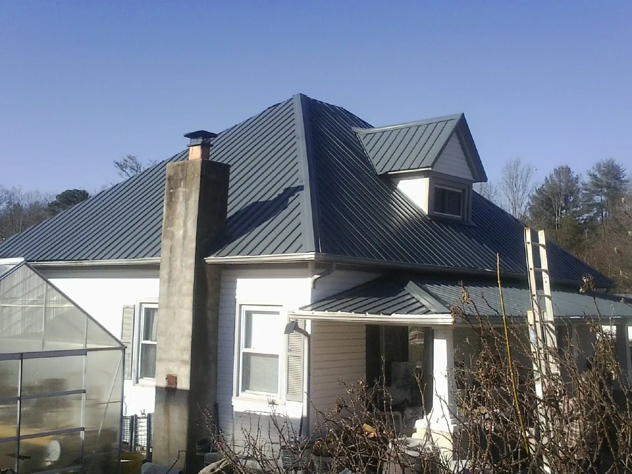 Dark blue standing seam metal roof on a white farmhouse with dormer — Slate & Tile Roof Repair by Roofing Brothers in Crump