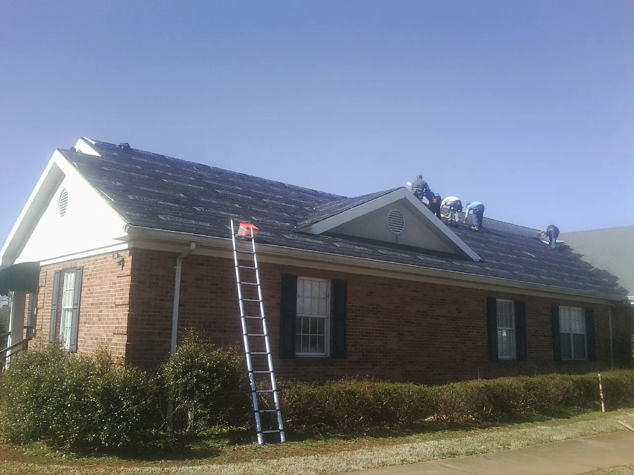 Crew tearing shingles off a brick ranch roof with a ladder set — Metal Roof Repair work by our crew in Crump