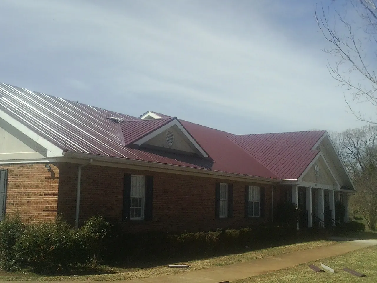 Red metal roof with gabled entries on a long brick building, from a Hail Damage Roof Repair job in Crump