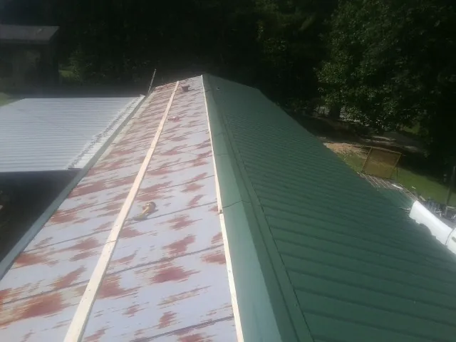 Old rusted panels beside newly installed green metal roofing — Wind Damage Roof Repair by Roofing Brothers in Crump