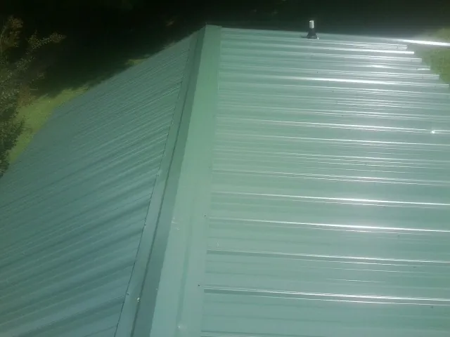 New green metal panels meeting at the ridge of a roof — Flat Roof Repair work by our crew in Crump