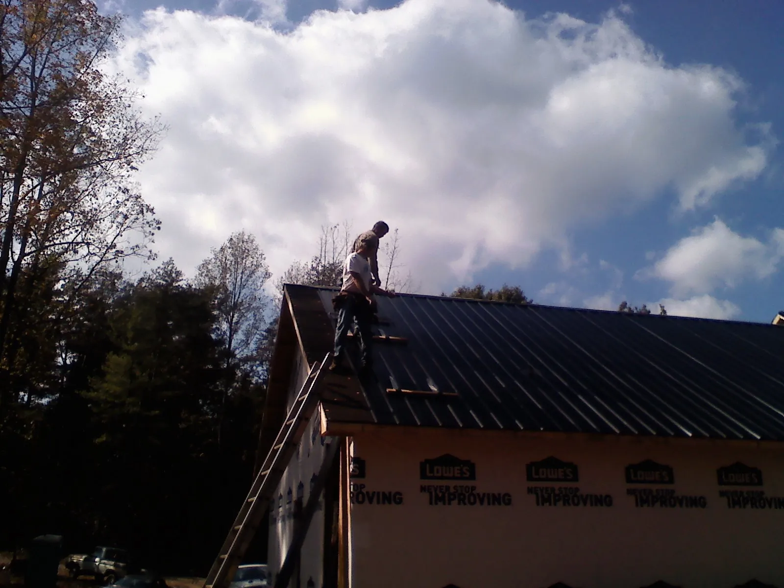 Roofer fastening dark metal panels high against a cloudy sky, from a Roof Inspection job in Crump