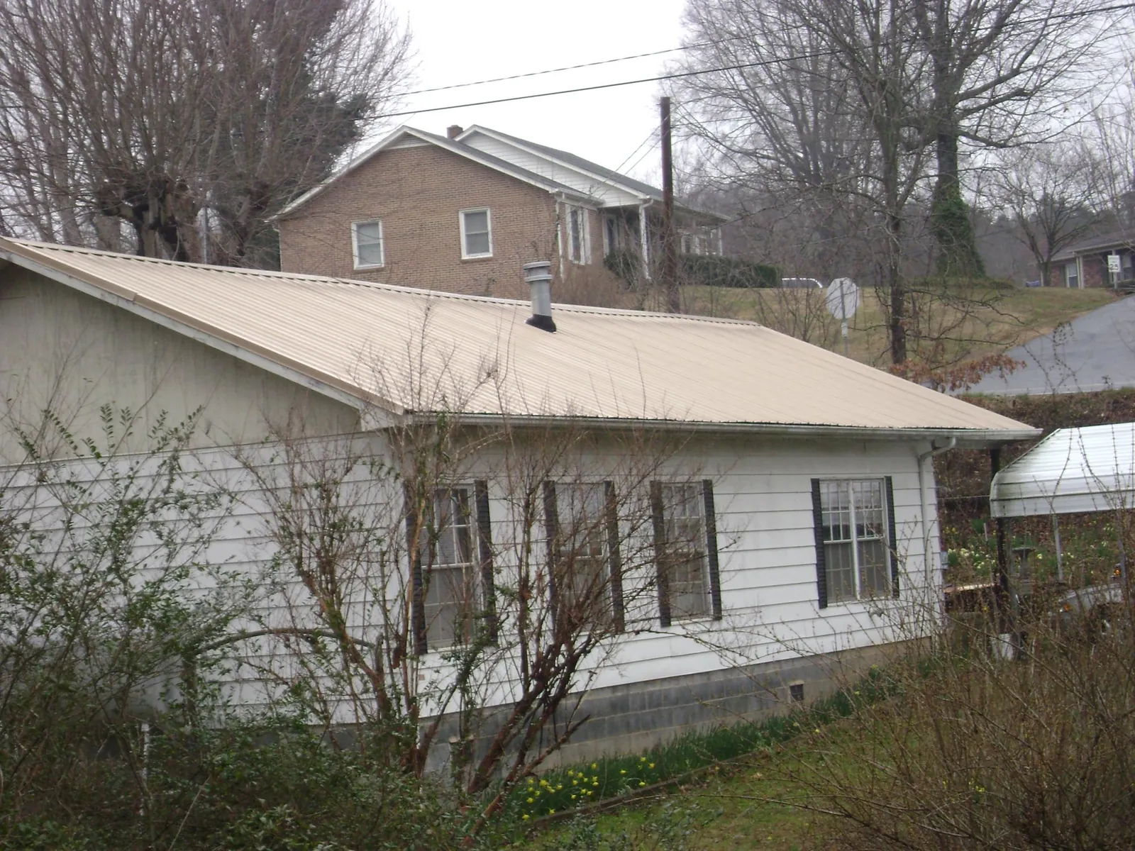Tan metal roof on a white sided house set into a hillside — Commercial Roofing by Roofing Brothers in Crump